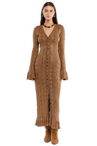 Mujer usando un vestido largo marrón con volados en el ruedo del cuerpo y en los puños .