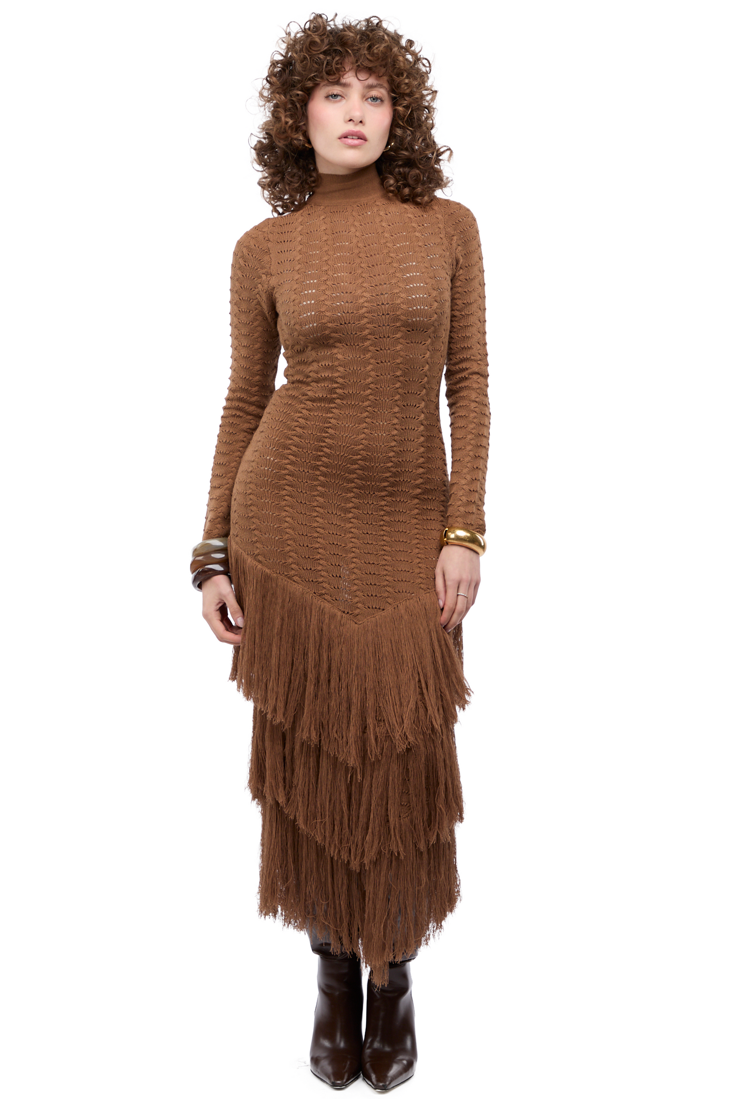 Mujer usando un maxi vestido tejido en marrón con mangas largas, escote versátil y tiras amarrables. Su faldón tiene tres capas de flecos.