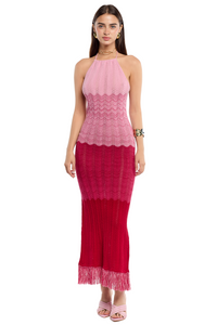 Mujer usando un maxi vestido tejido en tonos degradé con flecos en el ruedo y tirantes amarrables en el cuello.